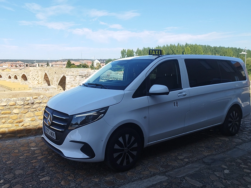 Taxi aparcado y de fondo muralla y pueblo del bierzo.